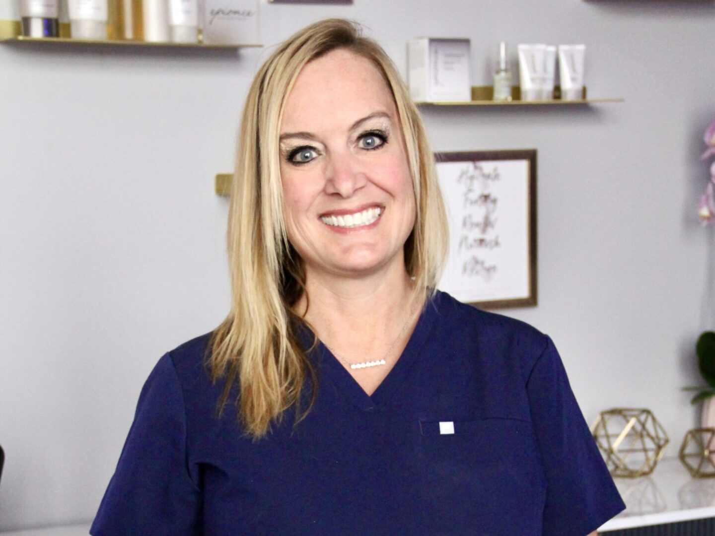 A woman in blue scrubs smiles for the camera.